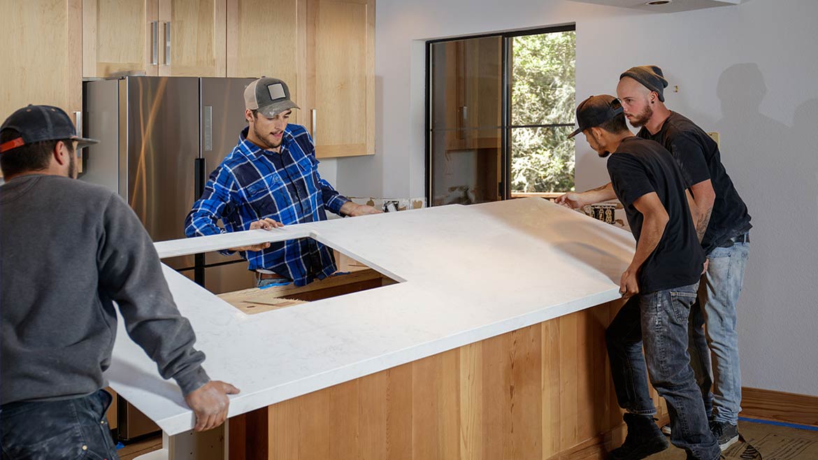 Four workers installing a stone countertop in a kitchen.