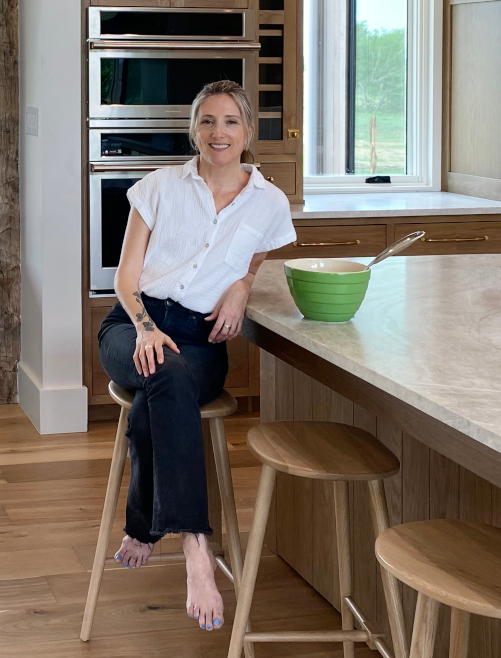 Juliet Whalen of Jibe Design sits on a bar stool leaning against the kitchen island.
