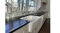 white farmhouse-style kitchen sink with a black roll-up drying rack on a black countertop. 