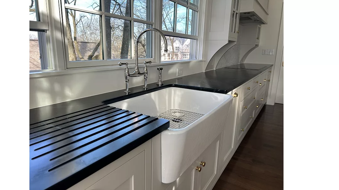 white farmhouse-style kitchen sink with a black roll-up drying rack on a black countertop.