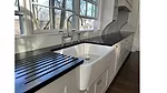white farmhouse-style kitchen sink with a black roll-up drying rack on a black countertop. 