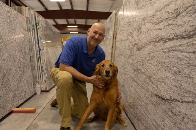 Tim Zeng in slab warehouse kneeling with his dog