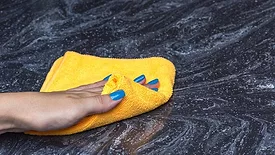 a person cleaning a dark, veined natural stone countertop