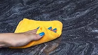 a person cleaning a dark, veined natural stone countertop